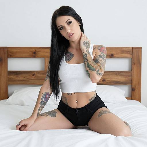 Tattooed Woman in White Crop Top and Black Shorts Sitting on Bed
