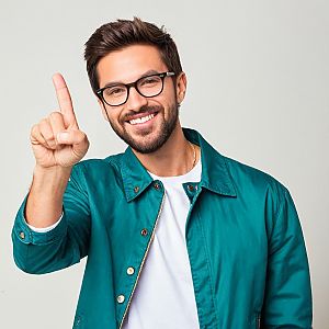 Cheerful man in teal jacket signaling number one
