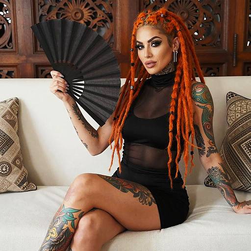 Woman with Orange Dreadlocks and Tattoos Holding Black Fan Sitting on Sofa