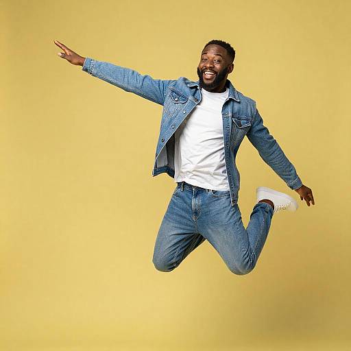 Joyful Young Man Jumping in Denim Outfit on Yellow Background