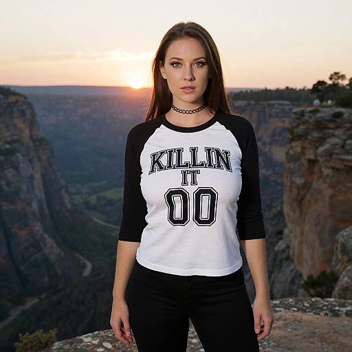 Woman Wearing Black and White Raglan Top with 'KILLIN IT 00' Text on Rocky Cliff Sunset