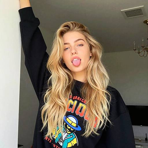 Playful Young Woman with Blonde Hair in Graphic Sweatshirt Indoor Pose