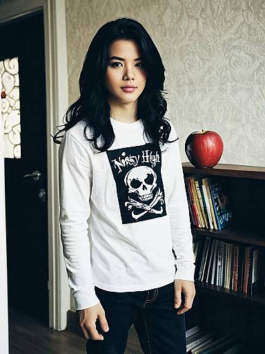 Portrait of Man in White Skull Graphic Shirt Standing by Bookshelf with Apple