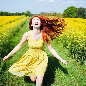 Joyful woman in yellow dress running through flowers