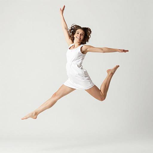Joyful Young Woman Jumping in White Dress Studio Shot