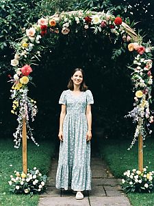 Young Woman in Floral Dress Standing Under Flower Arch in Garden