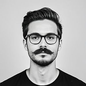 Close-up black and white portrait of a young man with glasses and a curled mustache