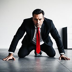 Determined Man in Black Suit with Red Tie Kneeling on Floor