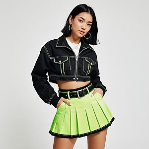Woman in Contemporary Streetwear Black Cropped Jacket with Contrast Stitching and Neon Green Pleated Skirt
