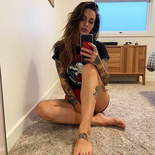 Tattooed Woman Sitting on Carpet Taking Mirror Selfie in Casual Outfit