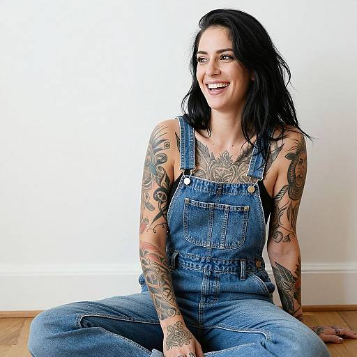 Smiling Tattooed Woman in Denim Overalls Sitting on Floor