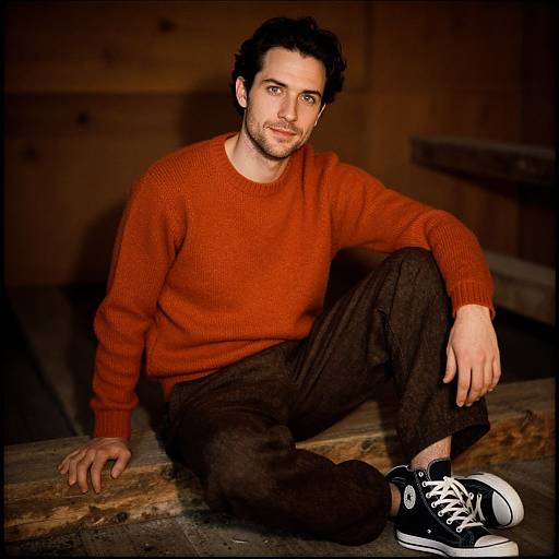 Young Man in Orange Sweater Sitting Indoors on Wooden Step