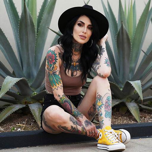 Tattooed Woman in Black Hat and Yellow Sneakers Sitting Outdoors