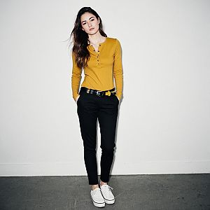 Young Woman in Mustard Yellow Shirt and Black Pants Standing Against White Wall