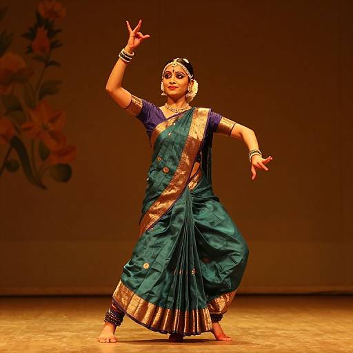 Photograph of a dancing woman in a teal and gold sari, blue blouse, and traditional jewelry, performing on a stage under warm lighting.