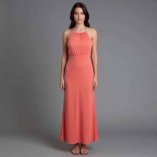 Photograph of a woman with long black hair, wearing a sleeveless, coral-colored, floor-length dress, standing against a plain gray background.