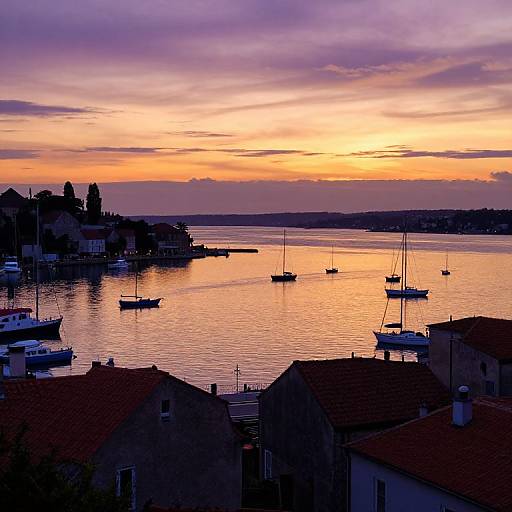 Photograph of a serene harbor at sunset, with vibrant orange and purple skies reflecting on calm water, silhouetted boats, and red-roof