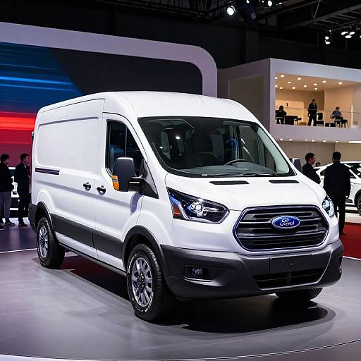 Photograph of a white Ford Transit van displayed in a brightly lit showroom with people in the background, illuminated by red and blue lighting.