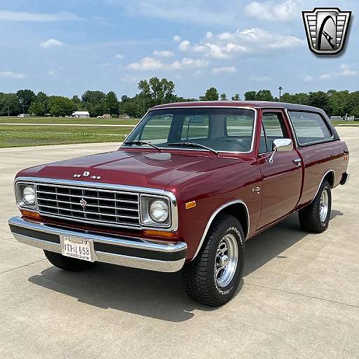 Photograph of a shiny maroon 1970s Chevrolet Nova sedan with chrome accents, parked on a concrete surface, under a blue sky. Logo