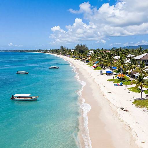 Aerial photograph of a tropical beach with white sand, turquoise water, small boats, palm trees, and colorful umbrellas under a bright blue sky.