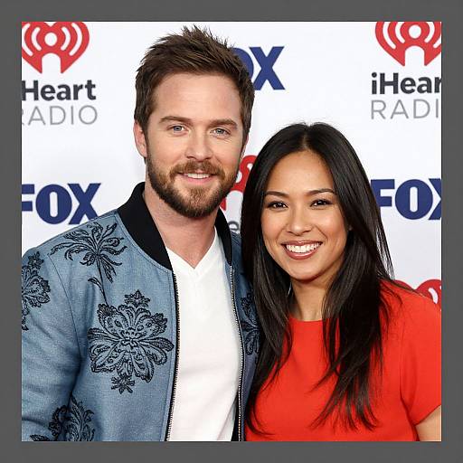 Photograph of a bearded white man with short brown hair in a blue floral jacket and a smiling Asian woman with long black hair in a red shirt