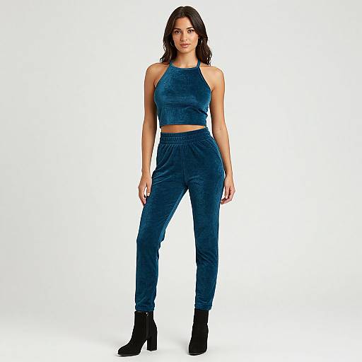 Photograph of a young woman with wavy dark hair wearing a blue velvet crop top and matching high-waisted pants, black ankle boots, standing
