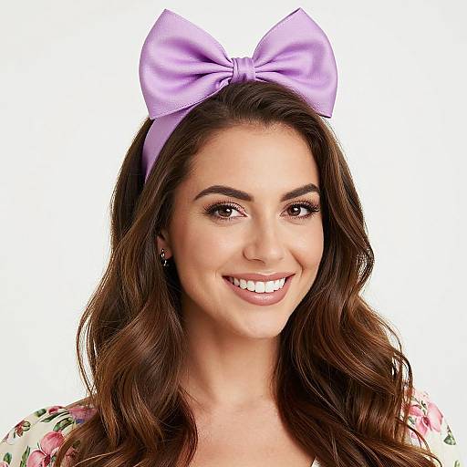Photograph of a smiling young woman with long brown hair, wearing a large lavender bow headband and floral dress, against a white background.
