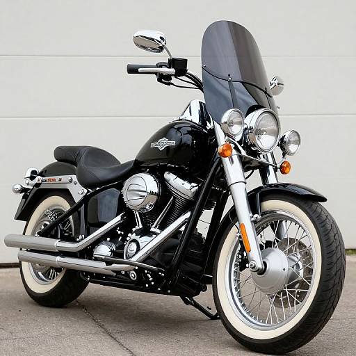 Photograph of a black cruiser motorcycle with chrome accents, white-walled tires, dual round headlights, and a tall windshield, parked against a white garage