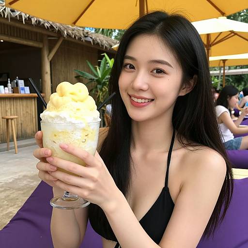 Photograph of a smiling Asian woman with long black hair, wearing a black bikini top, holding a creamy, swirled drink under a yellow umbrella