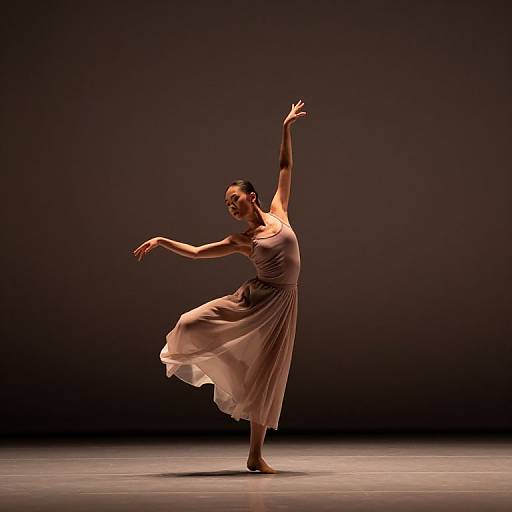 Photograph of a graceful dancer in a flowing, beige, sleeveless dress, performing a ballet pose with arms extended, against a dark, spotlighted