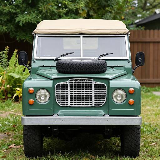 Photograph of a vintage green off-road vehicle with beige roof, black spare tire on hood, front grille, and orange lights, parked on grass with