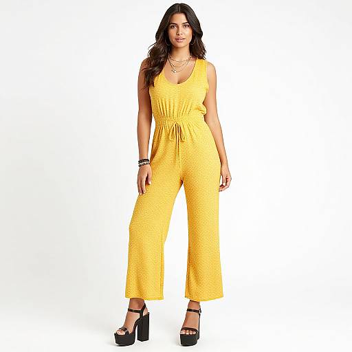 Photograph of a confident woman with long dark hair, wearing a bright yellow, lace-embroidered, sleeveless jumpsuit and black high heels