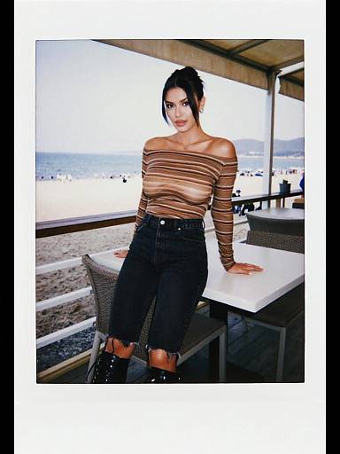 Photograph of a young woman with dark hair in an updo, wearing a brown striped off-shoulder top, black high-waisted shorts