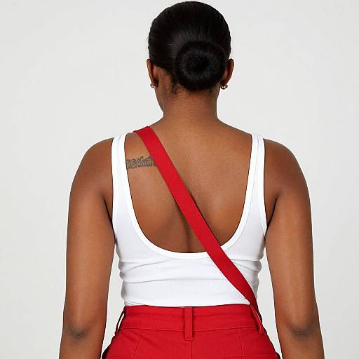 Photograph of a dark-skinned woman with black hair in a bun, wearing a white tank top and red pants, red strap across back, visible