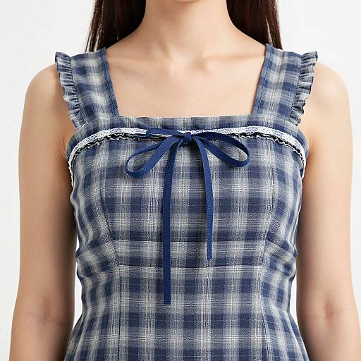 Photograph of a woman's upper body wearing a blue and white plaid sleeveless dress with ruffled straps and a small navy bow at the center
