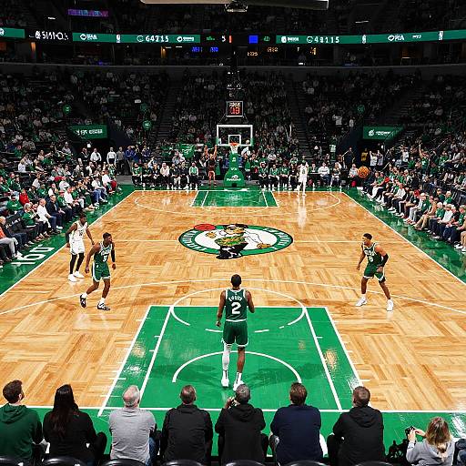 Photograph of a professional basketball game: two teams on a wooden court, with a packed stadium, scoreboard, and officials in the foreground.