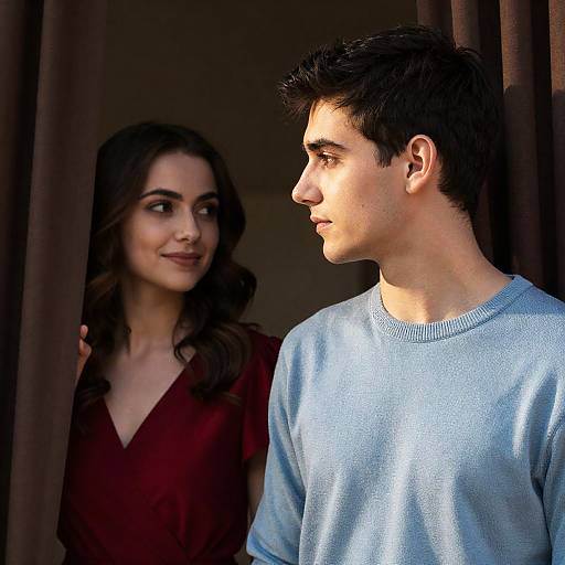 Photograph of a young couple standing in a doorway; woman with wavy dark hair in maroon top, man with short dark hair in light blue