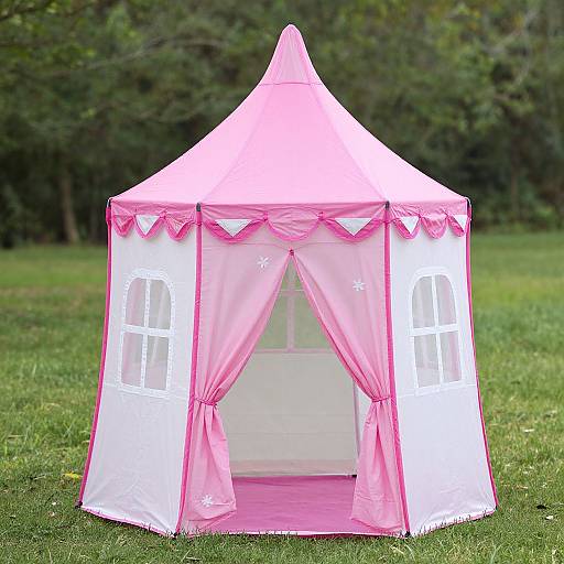 Photograph of a pink and white children's tent with pink curtains, white window frames, and a pointed pink roof, set on a grassy lawn