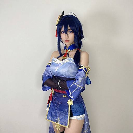 Photograph of a fair-skinned woman in elaborate blue and white cosplay outfit with black hair, red ribbon, and gold accessories, standing against a plain