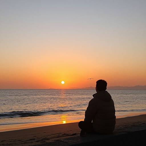 Photograph of a silhouetted person sitting on a beach, watching a vibrant orange and blue sunset over the ocean.