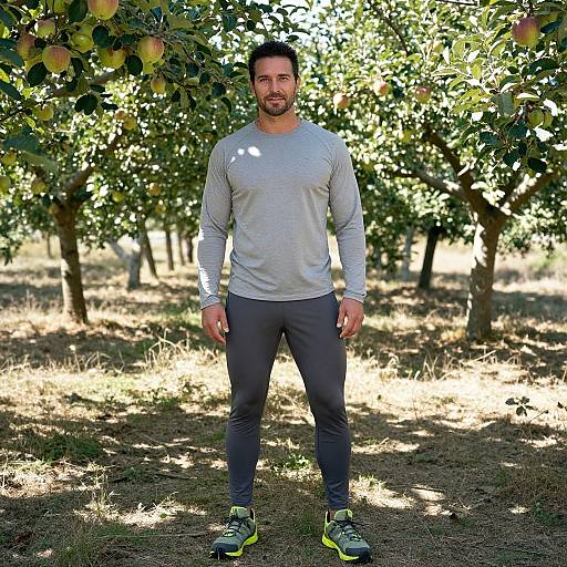 Photograph of a bearded, muscular man with short dark hair, wearing a grey long-sleeve shirt, black leggings, and yellow-green sneakers