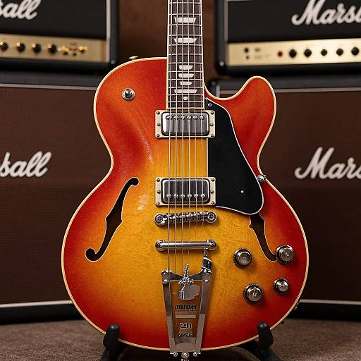 Photograph of a sunburst electric guitar with black pickguard and knobs, standing in front of stacked Marshall amplifiers.