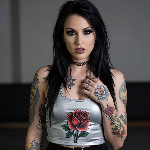 Photograph of a tattooed woman with long black hair, wearing a silver tank top with a red rose, choker, and dark makeup, standing