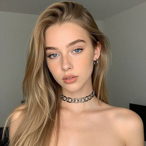 Photograph of a young, fair-skinned woman with long, light brown hair, blue eyes, and a black choker necklace, looking directly at