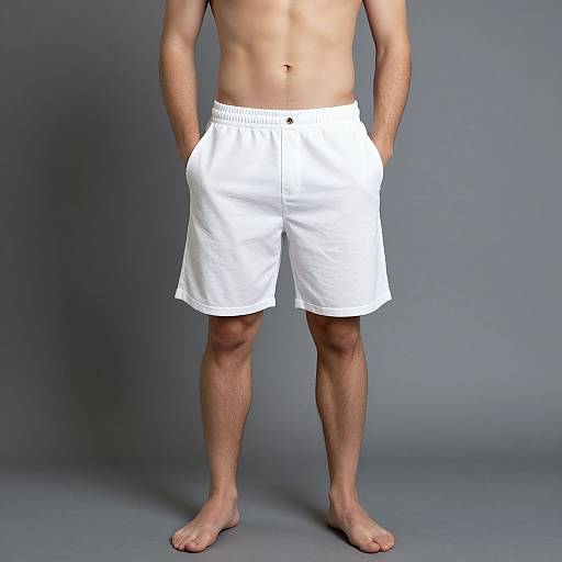 Photograph of a shirtless, light-skinned man standing barefoot, wearing white, knee-length shorts with hands in pockets, against a gray background
