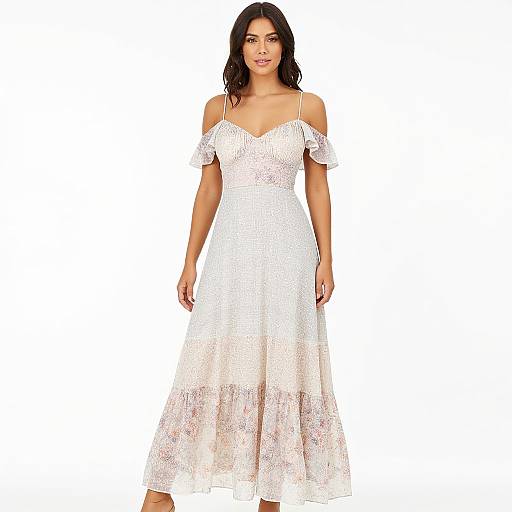 Photograph of a smiling woman with long dark hair, wearing a white off-shoulder, lace, ankle-length dress, standing against a plain white