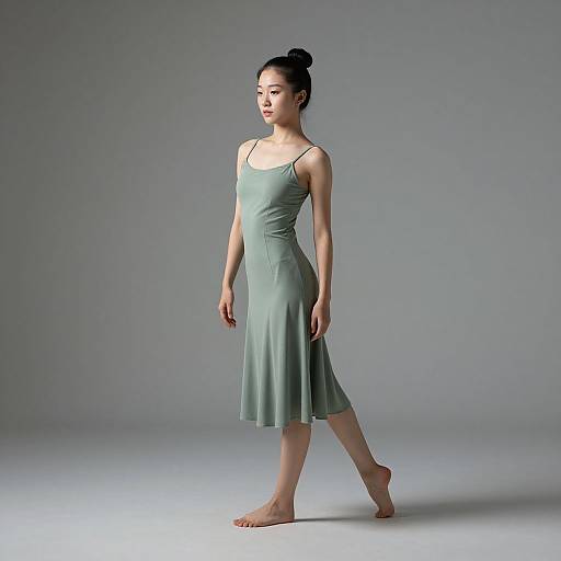Photograph of an East Asian woman with black hair in a bun, wearing a mint green, sleeveless, knee-length dress, walking barefoot on