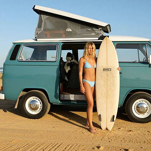 Photograph of a blonde woman in a blue bikini, holding a surfboard, standing beside a turquoise vintage van on a sandy beach.