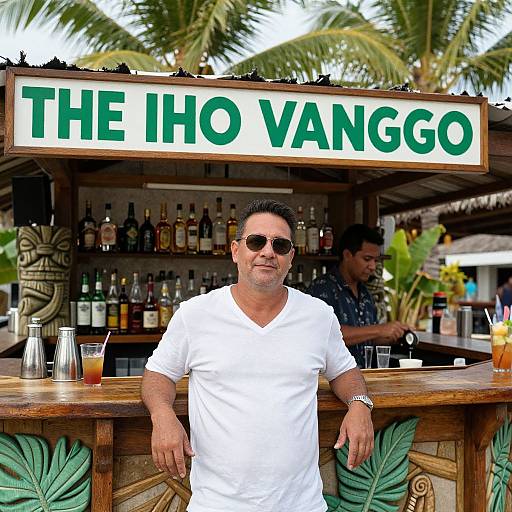 Photograph of a middle-aged man with short dark hair, sunglasses, and white shirt, standing in front of a tropical bar with 