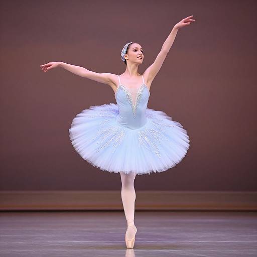 Photograph of a ballet dancer in a sparkling white tutu, poised on pointe, with arms gracefully extended, against a dark stage backdrop.